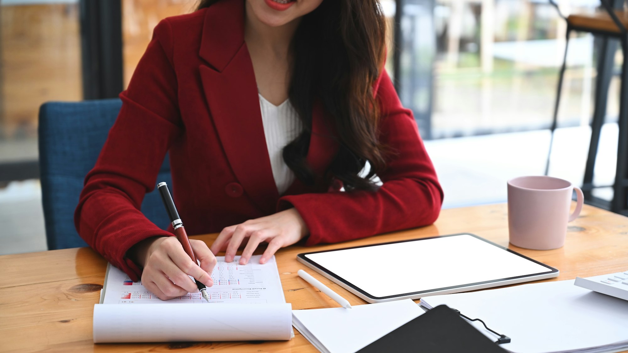 Successful businesswoman sitting at office desk and writing in formation on document.