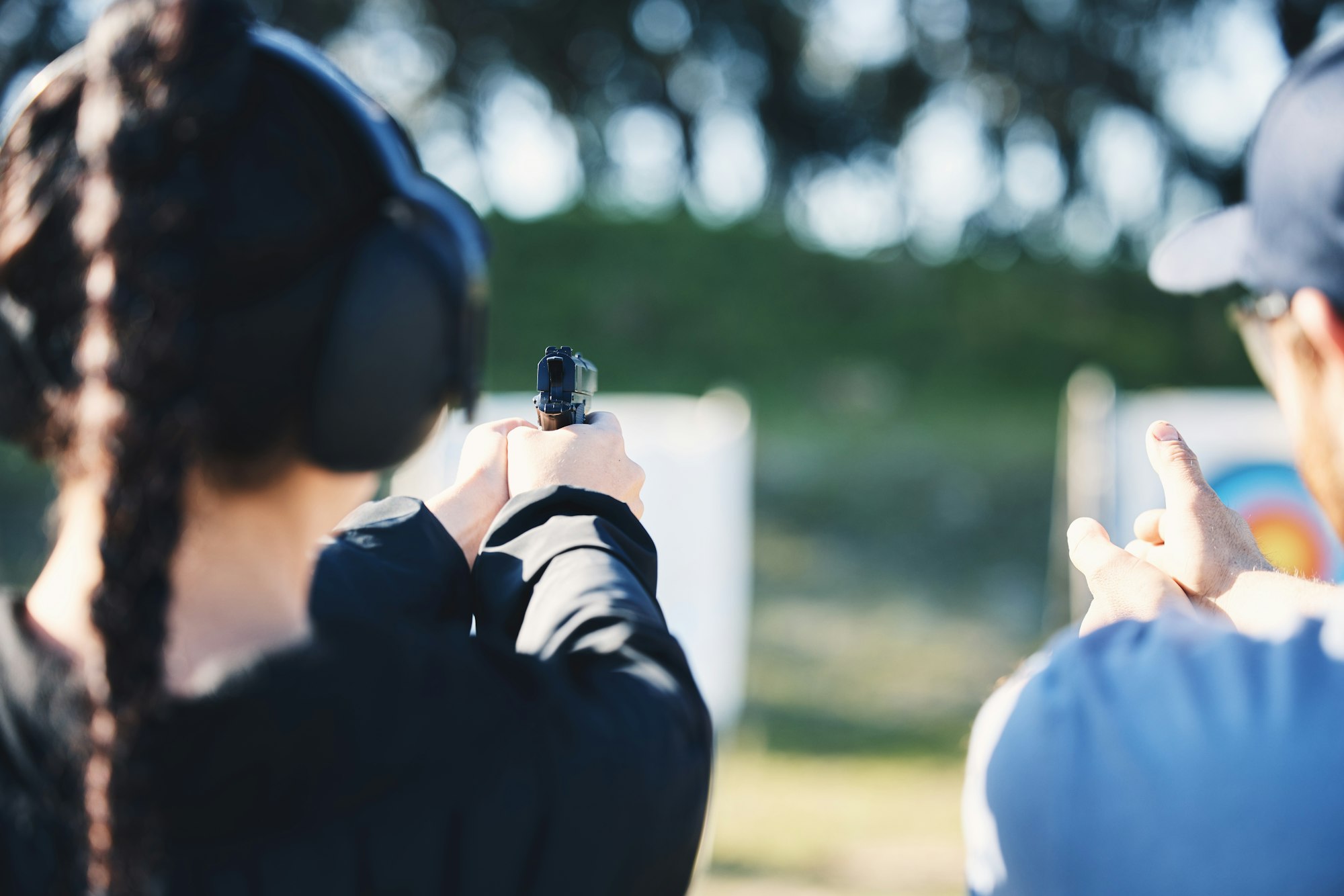 Woman, gun and learning to shoot with instructor at shooting range outdoor for target training. Saf